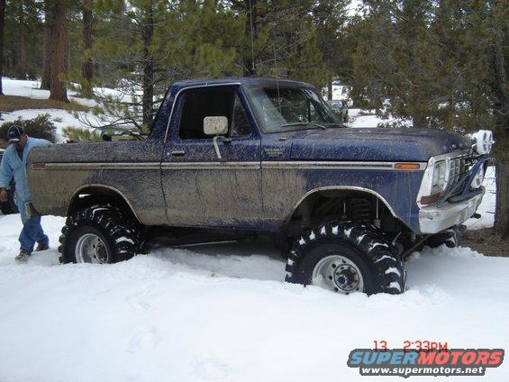 Blue Ford pickup truck with large off-road tires stuck in snow, side view