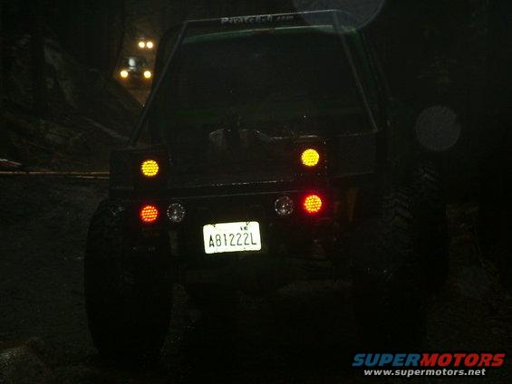 Rear view of an off-road SUV with its brake lights on, driving in the dark. Another vehicle is visible ahead