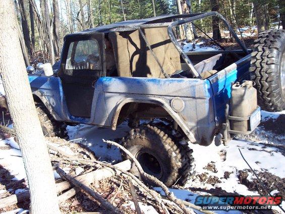 Blue 1974 Ford Bronco with roll cage and spare tire, stuck in mud and snow