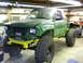 1990 Ford Bronco - Modified pickup truck with large tires and yellow frame, seen in a garage with visible tools and shelving.