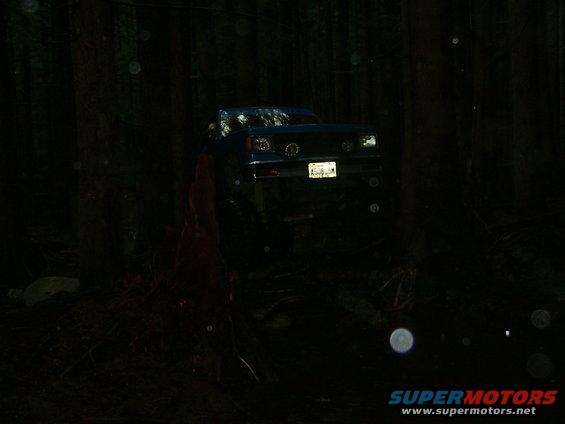 Blue SUV with a lifted suspension driving off-road at night. License plate is visible
