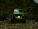 1990 Ford Bronco - A green off-road vehicle navigates a rocky stream bed surrounded by dense foliage.