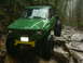 1990 Ford Bronco - This heavily modified off-road vehicle tackles a challenging rocky path through a dense, wet forest.