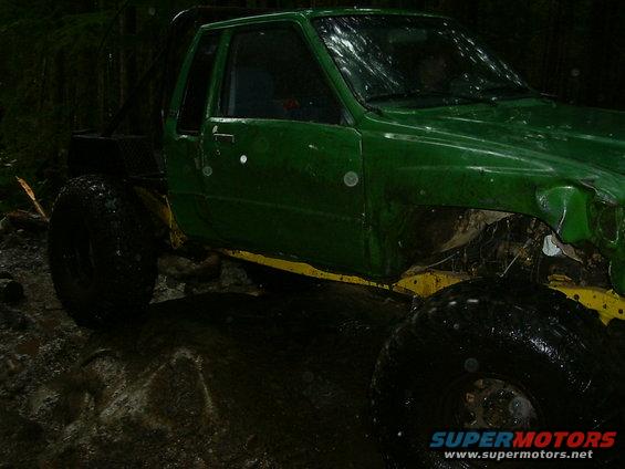 green off-road truck with large tires, in a muddy wooded area