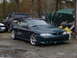 1995 Ford Mustang - A dark green Ford Mustang is parked outside next to other vehicles and covered items.