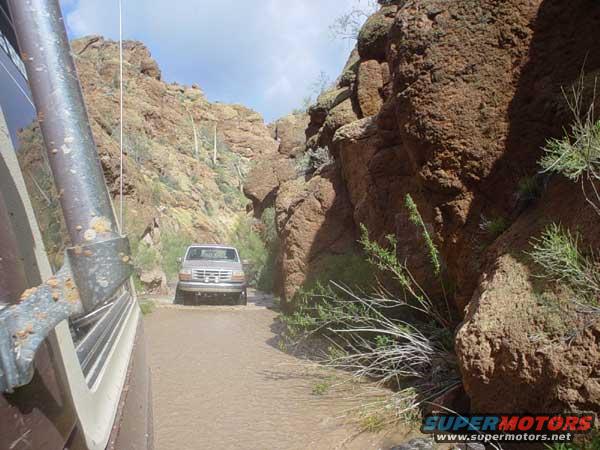Silver Ford Bronco driving through a muddy canyon road