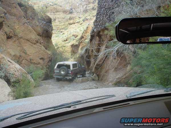 1989 Ford Bronco rear view driving through a rocky canyon stream
