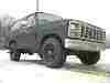 1985 Ford Bronco - A dark green Ford truck is viewed from the front three-quarter angle under an overcast sky.