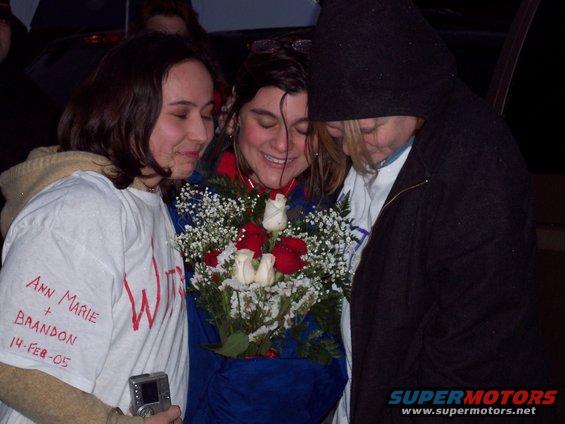 Three people embrace over a bouquet of red and white roses