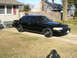 1999 Ford Crown Victoria - A black sedan is parked on a driveway in front of a house.