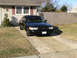 1999 Ford Crown Victoria - A black 1999 Ford Crown Victoria is parked in a driveway in front of a house.