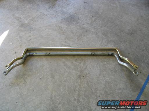 Two metal bars, one above the other, on a concrete floor. The top bar is gold-colored, the bottom is silver and shows wear