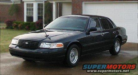 Black sedan parked in driveway, front quarter view. Has aftermarket wheels