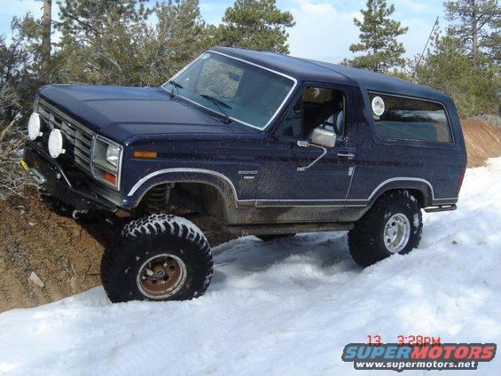 Dark blue Ford Bronco with large tires driving in snow
