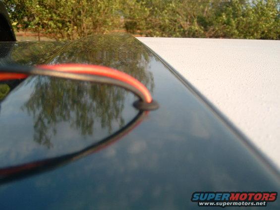Dark car roofline with red and black wires exiting a grommet, reflecting trees