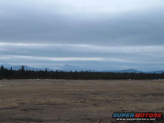 Landscape view of a field, forest, and mountains under a cloudy sky