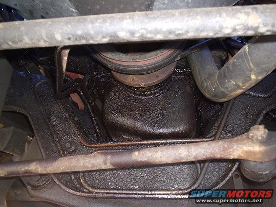 Underside of a vehicle with an oily engine oil pan and rusty suspension parts