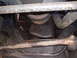 1985 Ford Bronco - The underside of a vehicle reveals an oily engine oil pan and corroded suspension components.