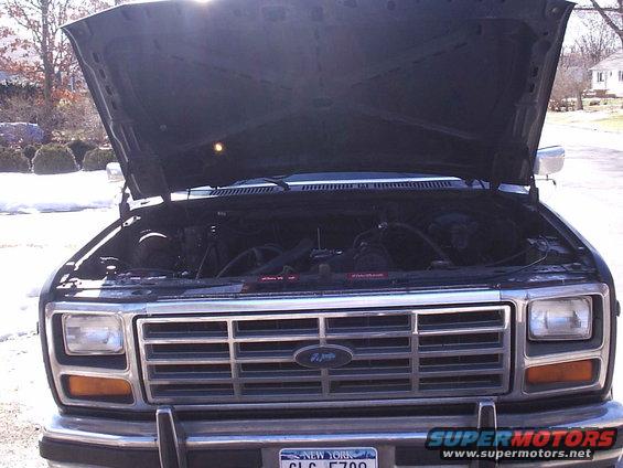 Front view of a dark-colored Ford Bronco with hood open, showing engine and grille