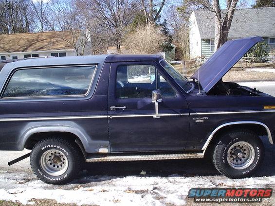 Side view of a dark blue Ford Bronco with a grey top, hood open. BFGoodrich All-Terrain T/A tires visible