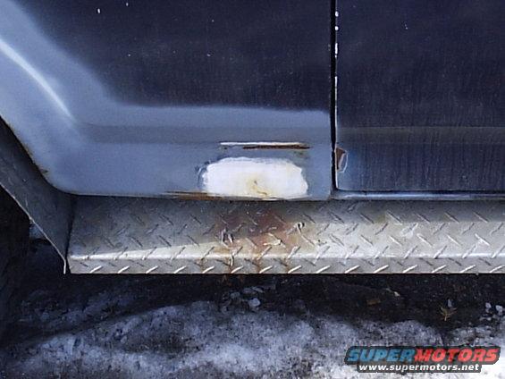 Dark blue vehicle lower body panel with rust and a patch, above a diamond plate step