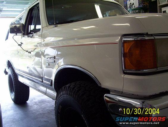 White Ford Bronco parked in a garage, showing the front fender and headlight