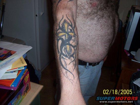 Tattoo of a cross with tribal elements on a hairy arm