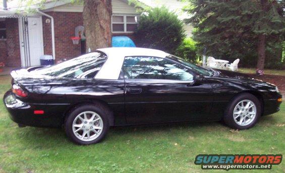 Black 2001 Chevrolet Camaro with a white t-top, parked on grass in front of a house