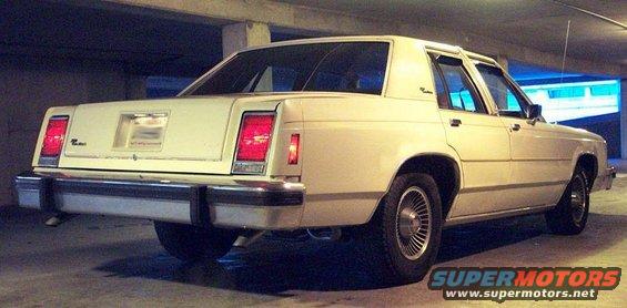 Rear view of a cream-colored 1983 Ford sedan parked indoors. It has rectangular taillights and chrome bumpers