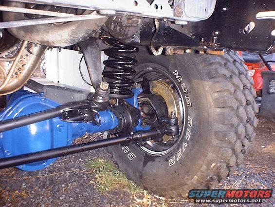 Close-up of a blue front axle, black suspension components, and a large off-road tire with 'MUD ROVER' text