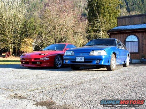 Red Ford Probe and blue Ford Mustang parked outside a building