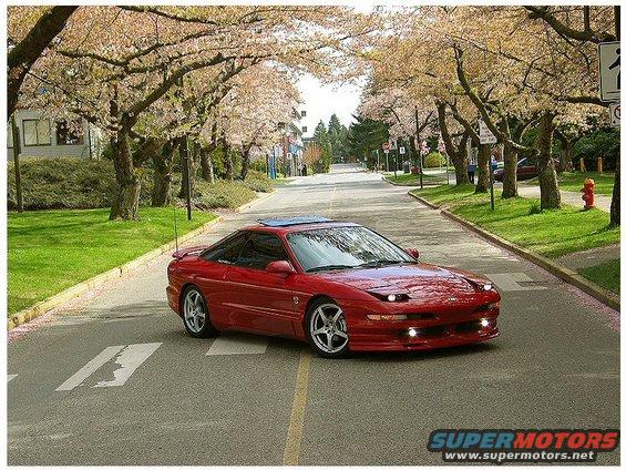 Red sports car with a sunroof, driving on a tree-lined street during springtime