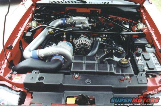 Engine bay with a large turbocharger and intercooler piping. The car is red