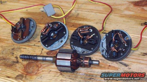 Several disassembled window motors and a motor armature with wires on a wooden surface