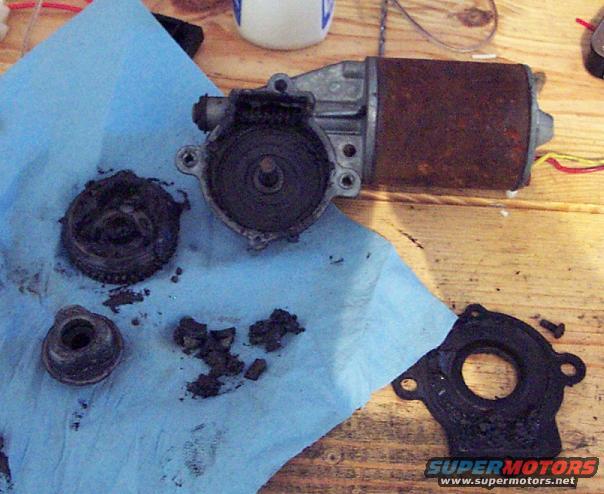 Disassembled window motor with rusty cylinder and gears on blue paper towel