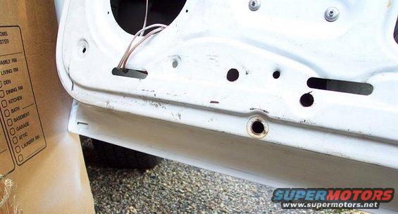 Inside of a car door, showing wiring and mounting holes. A cardboard box with room labels is on the left