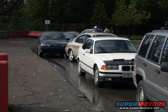 White BMW 3-series coupe with black hood bra, license plate IZ 1 E, parked on wet asphalt