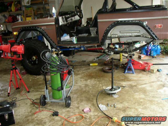 1970s Ford Bronco with fender removed, undergoing repairs in a garage with welding equipment and tools