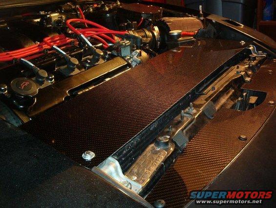 Engine bay showing red spark plug wires and carbon fiber covers over engine components