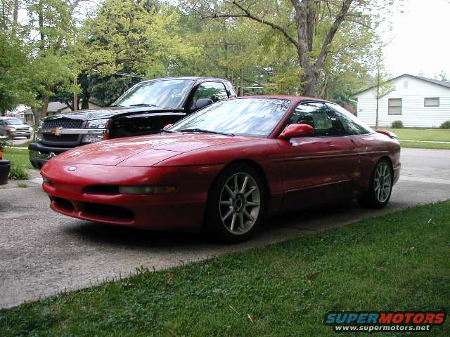 Red 1994 Ford Probe parked next to a black Chevrolet Silverado truck