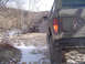 1979 Ford Bronco - Two off-road vehicles navigate a snowy, wooded path during daylight.