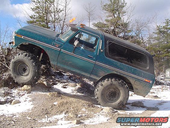 1979 Ford Bronco with large tires climbing over rocks and snow