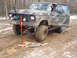 1979 Ford Bronco - A camouflage-painted Ford Bronco is stuck in the mud, with a hi-lift jack positioned to help free it.