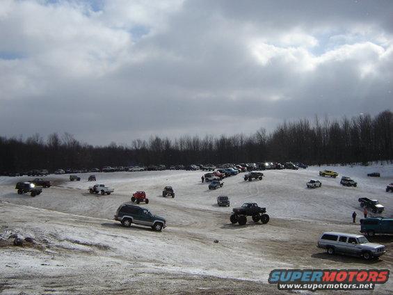 Many trucks and SUVs on a snow-covered field under a cloudy sky