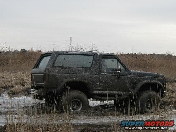 Mud-covered 1985 Ford Bronco stuck in a muddy field