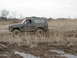1985 Ford Bronco - Ford Bronco navigating a muddy terrain with tall grass, kicking up mud.