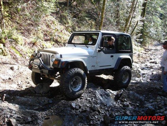 White Jeep Wrangler TJ navigating a rocky off-road trail with two people inside
