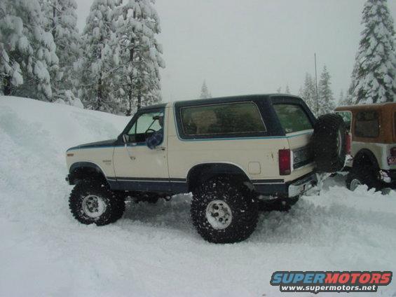 1986 Ford Bronco with external spare tire in snow, another vehicle partially visible behind it