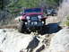 1990 Ford Bronco - A red Jeep CJ-7 navigates a rocky off-road path, with another Jeep visible in the background.