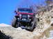 1990 Ford Bronco - This off-road vehicle navigates a challenging rocky path under a clear blue sky.